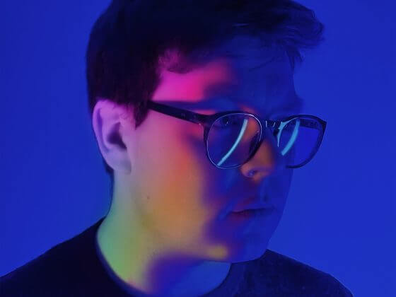 man with glasses with rainbow light on his face against a blue background.