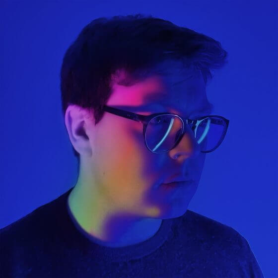 man with glasses with rainbow light on his face against a blue background.